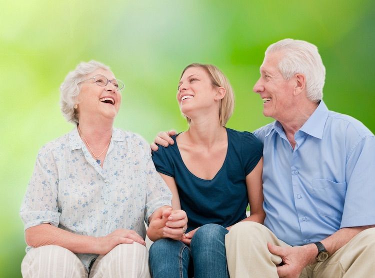 Eine jüngere Frau sitzt zwischen zwei älteren Personen und alle drei lachen