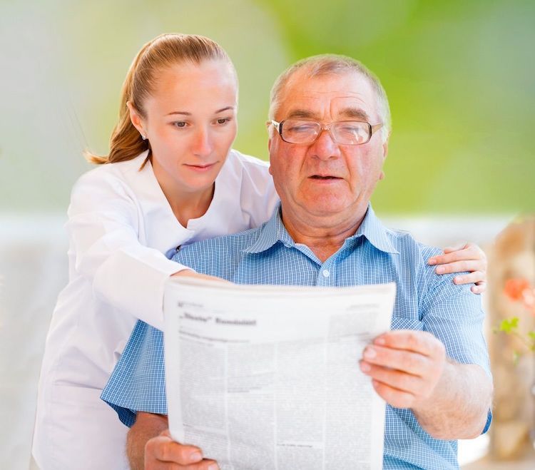 Betreuerin unterstützt älteren Mann beim Zeitung lesen